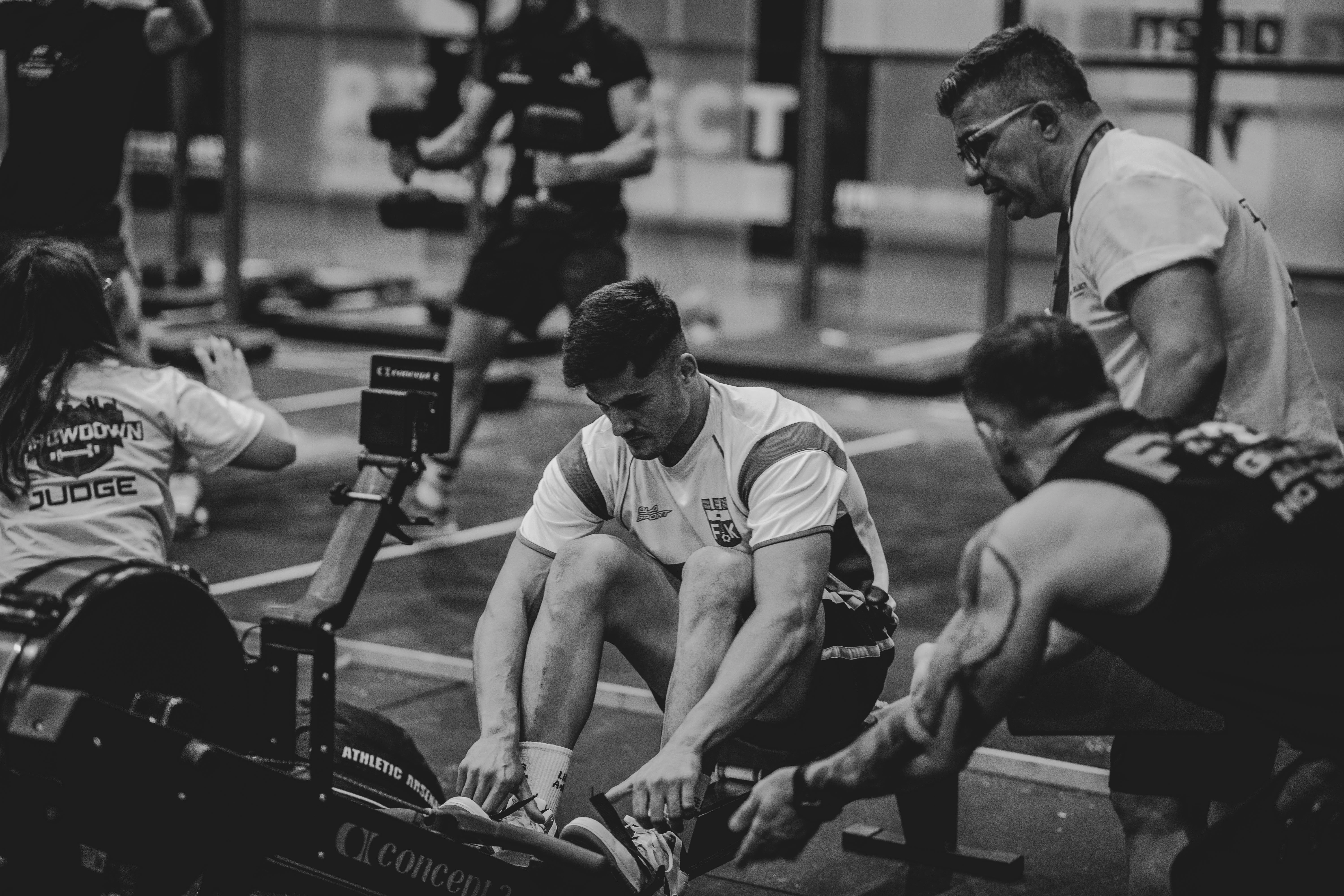 Man rowing indoors surrounded by his training team