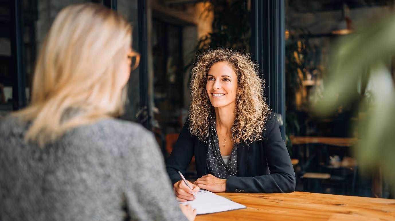 Professional nutritionist smiling while consulting with a client at a wooden table, discussing personalised nutrition plans in a bright, modern wellness office.