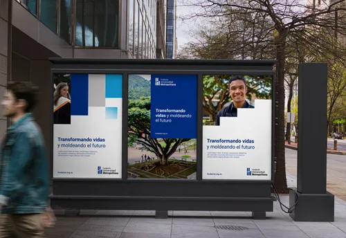 Three urban billboard posters displaying 'Transformando vidas y moldeando el futuro' with images of a woman and a man in graduation attire, and a nature scene in the center poster. The background shows a city street with blurred pedestrians walking by.