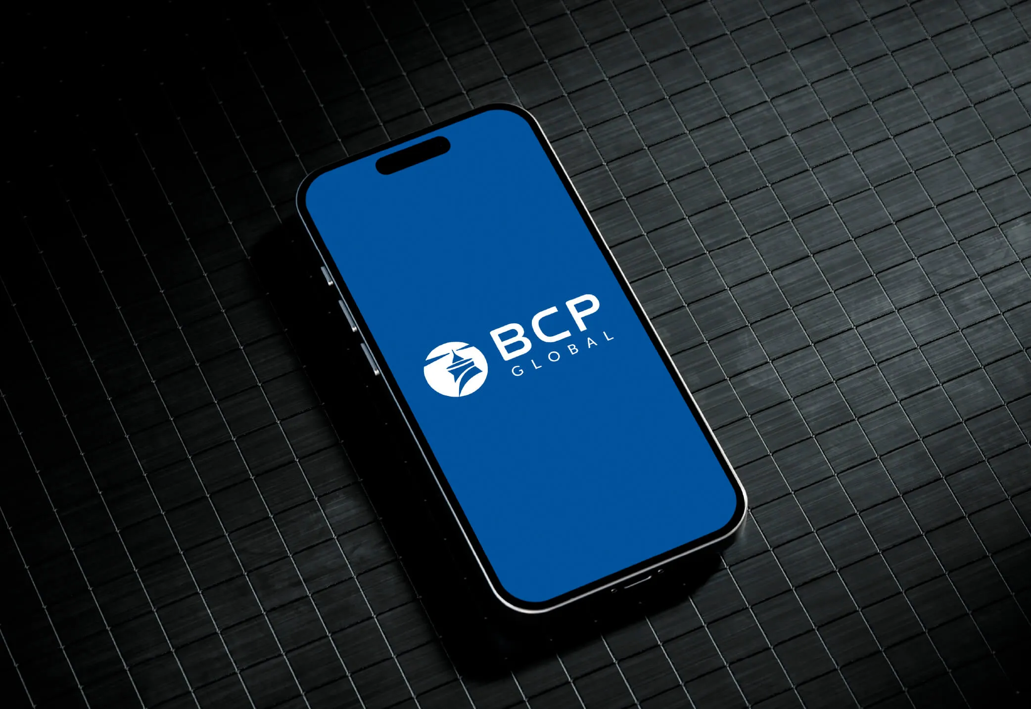 Smartphone displaying the BCP Global logo on a blue screen, placed on a textured dark surface.