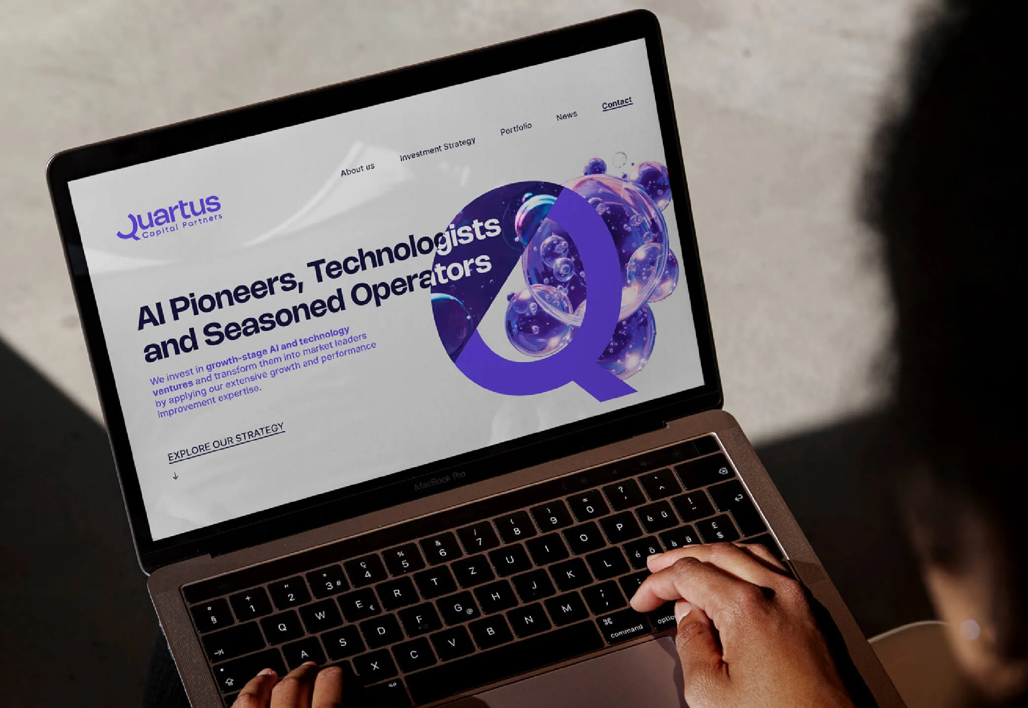 Person typing on a MacBook Pro laptop displaying Quartus Capital Partners website with headline about AI pioneers and investment strategy.
