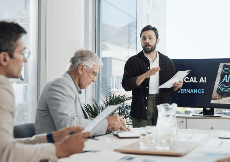 Man standing and presenting AI technology to two seated men reviewing documents in a modern office.