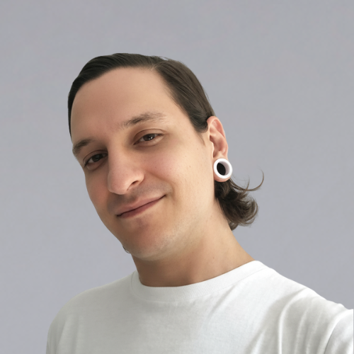 Smiling person with dark hair pulled back wearing white shirt and white circular earrings against a plain gray background.
