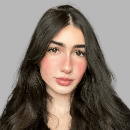 Gaby Gallo, content manager, young woman with long dark hair and natural makeup against a plain gray background.