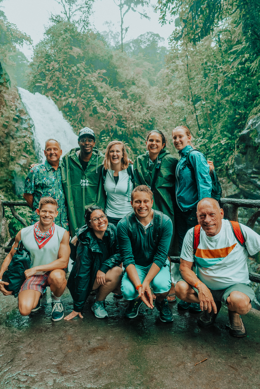 A group of people posing for a picture in front of a waterfall.