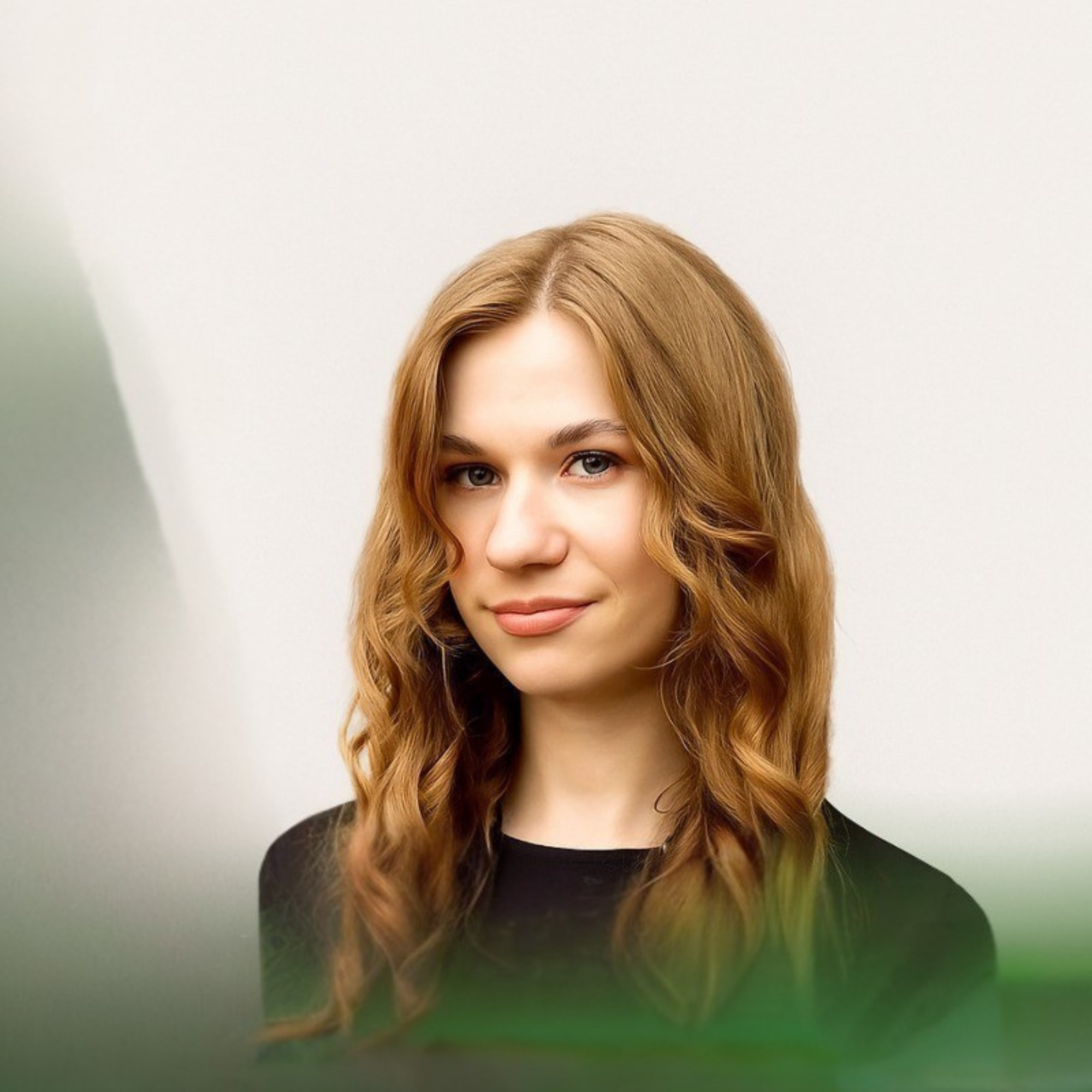 Portret młodej kobiety o długich, falowanych jasnobrązowych włosach i delikatnym uśmiechu na jasnym tle.