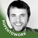Uśmiechnięty mężczyzna z krótkimi ciemnymi włosami na jasnym tle z zielonym kółkiem i napisem #OPENTOWORK.