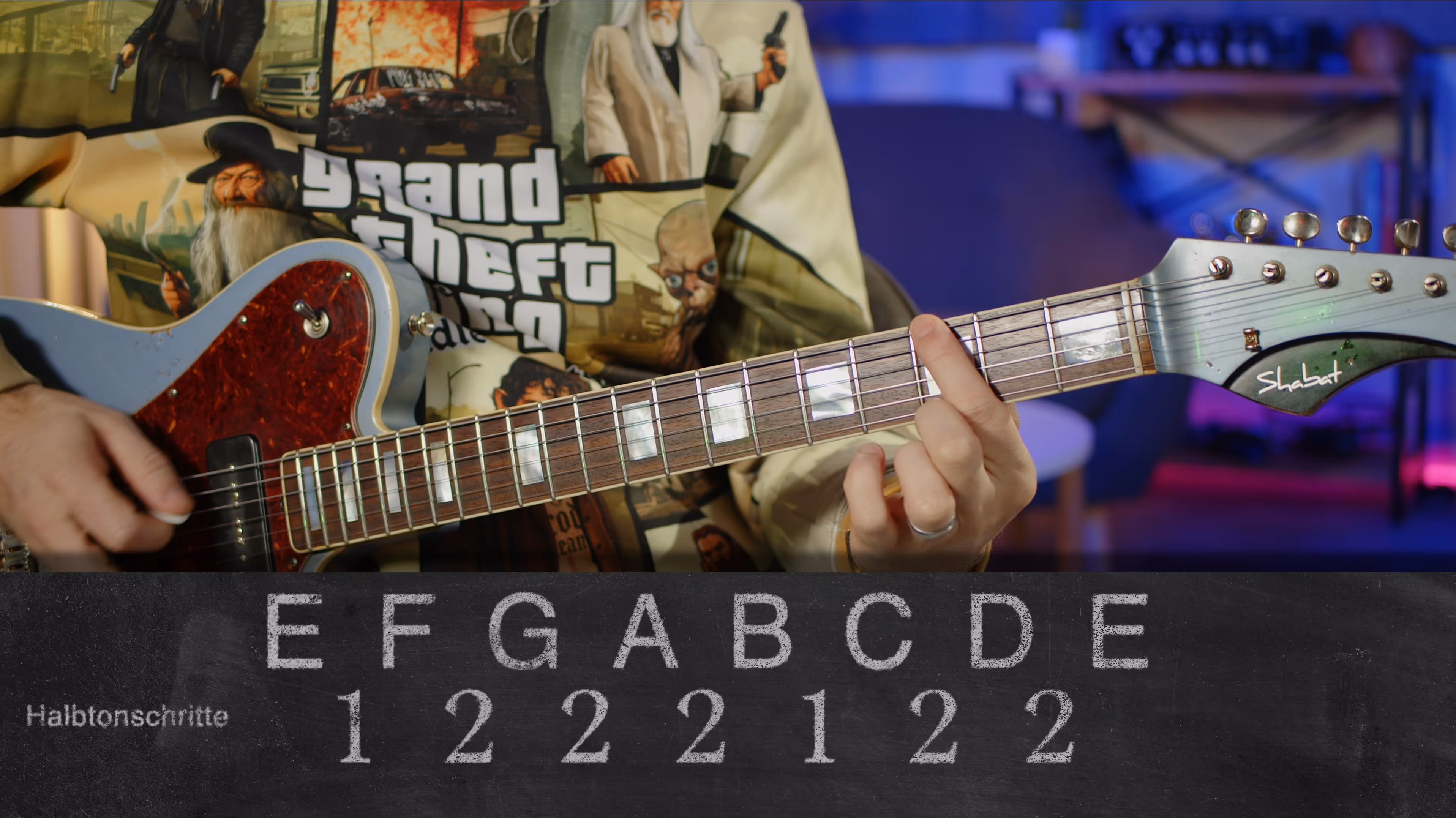 Person spielt elektrische Gitarre, im Hintergrund ein Bild mit Grand Theft Auto-Motiv und darunter eine Tafel mit Tonleiterschritten in Halbtonschritten.