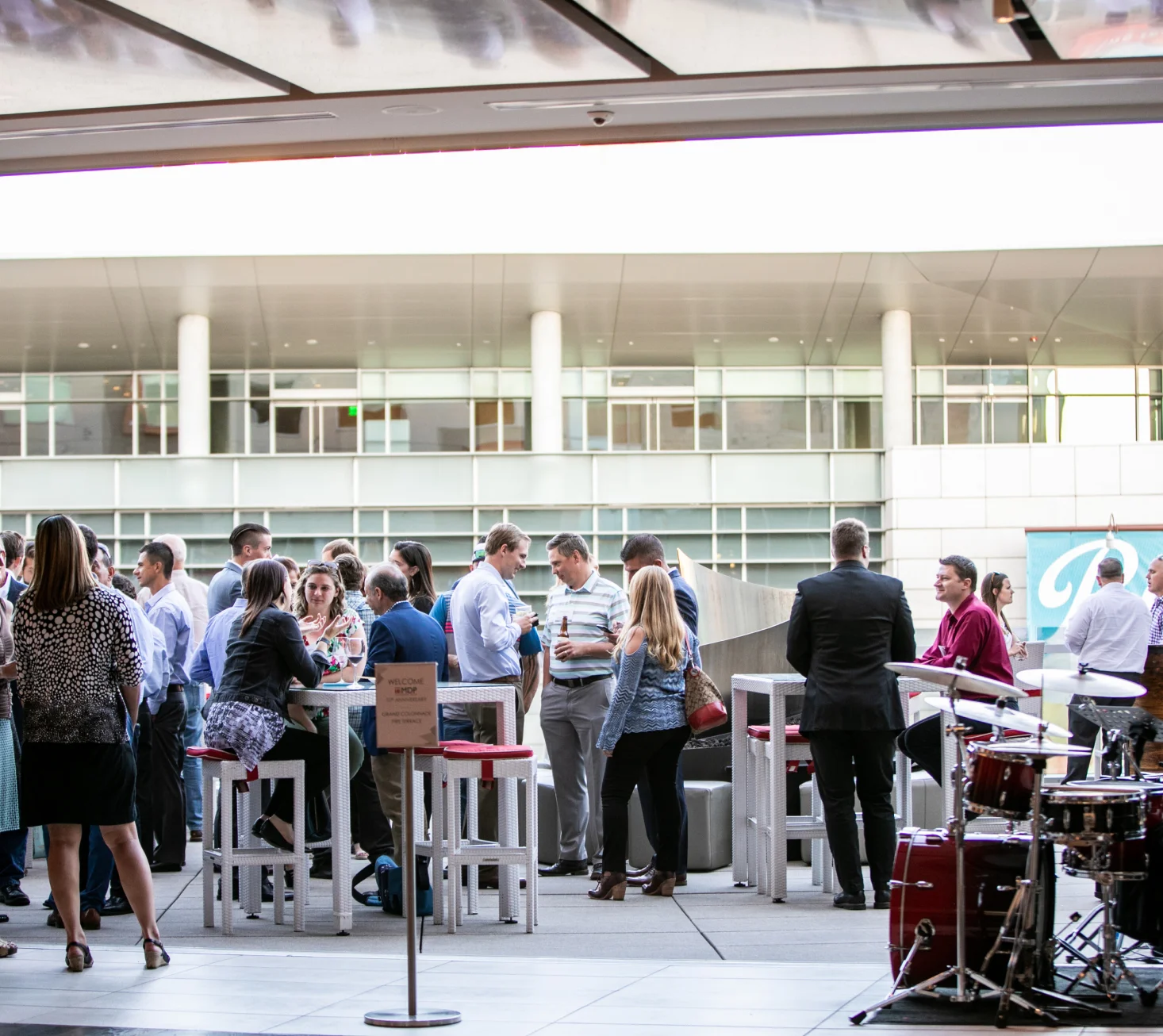 Business professionals networking at an outdoor corporate event with a modern building in the background and a live band setup.