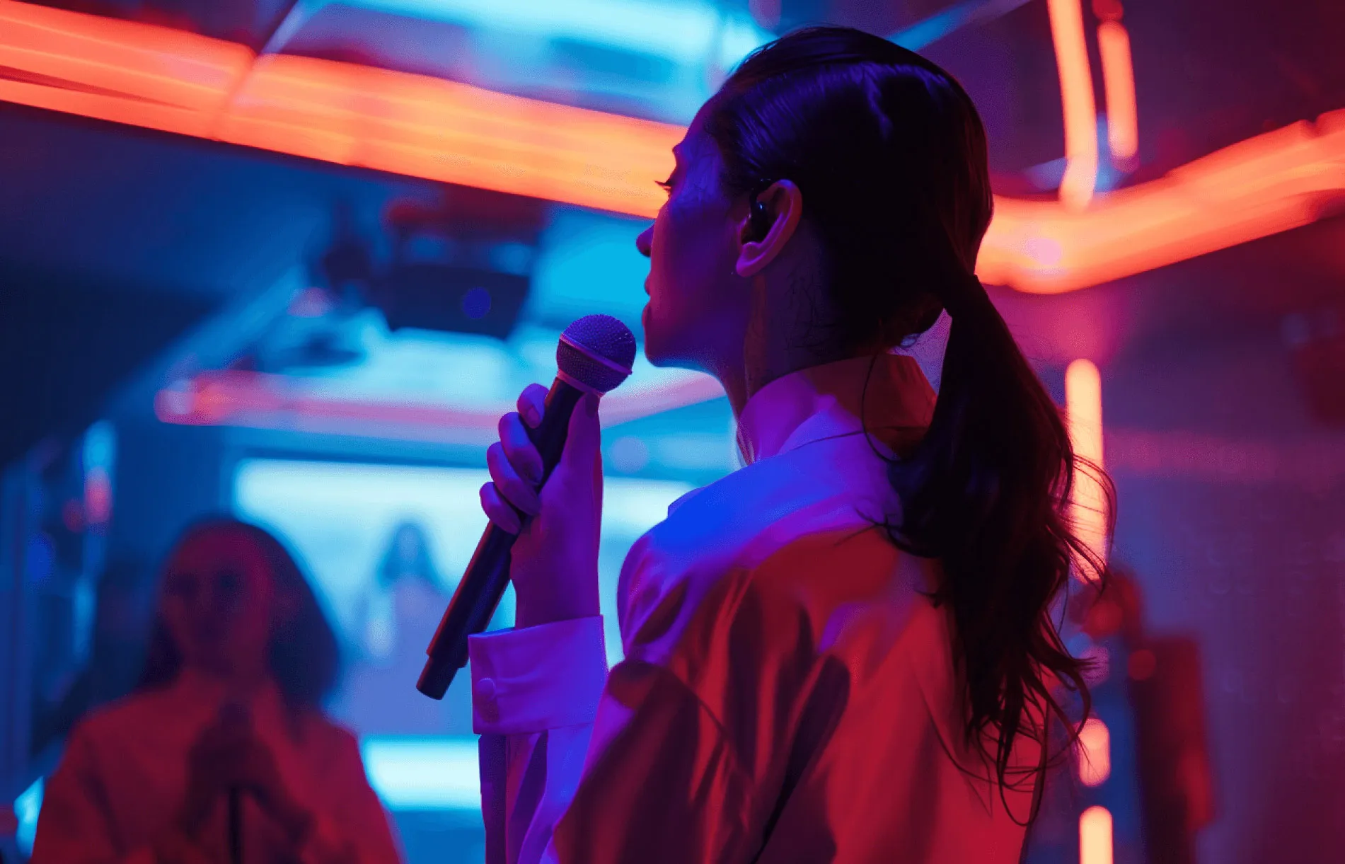 A person is standing with a mic and singing in a karaoke room filled with blue, purple and yellow colours coming from the room lighting