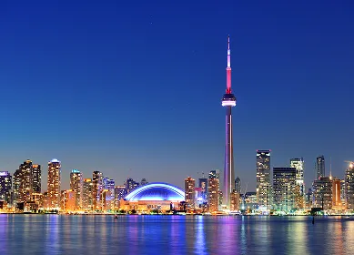 Toronto skyline at dusk with illuminated CN Tower and city lights reflected on water.