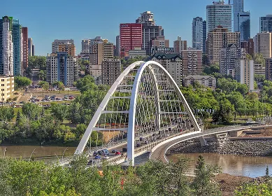 White arch bridge crossing a river with a city skyline in the background under a clear blue sky.