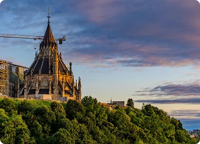 Evening aerial view of Ottawa downtown with illuminated Parliament Hill and Château Laurier hotel.