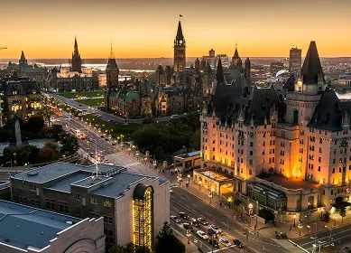 Evening aerial view of Ottawa downtown with illuminated Parliament Hill and Château Laurier hotel.