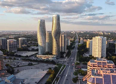 A cityscape view featuring three uniquely shaped high-rise buildings under a partly cloudy sky, with roads and other buildings around.