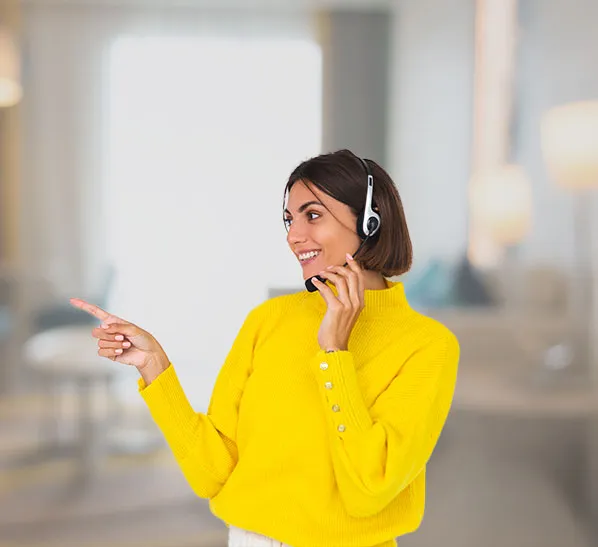 A smiling woman with a dark bob haircut wears a headset and a bright yellow sweater while pointing toward the left side of the frame.