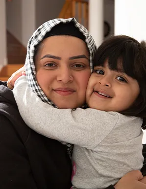 Close-up portrait of a smiling woman wearing a checkered hijab receiving a warm hug from a young child