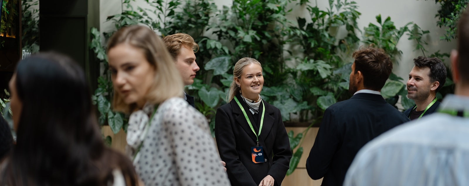 Green wall networking Guests mingling at the NORNORM and TechnologyWithin flex retention event, with a lush green plant wall in the background.