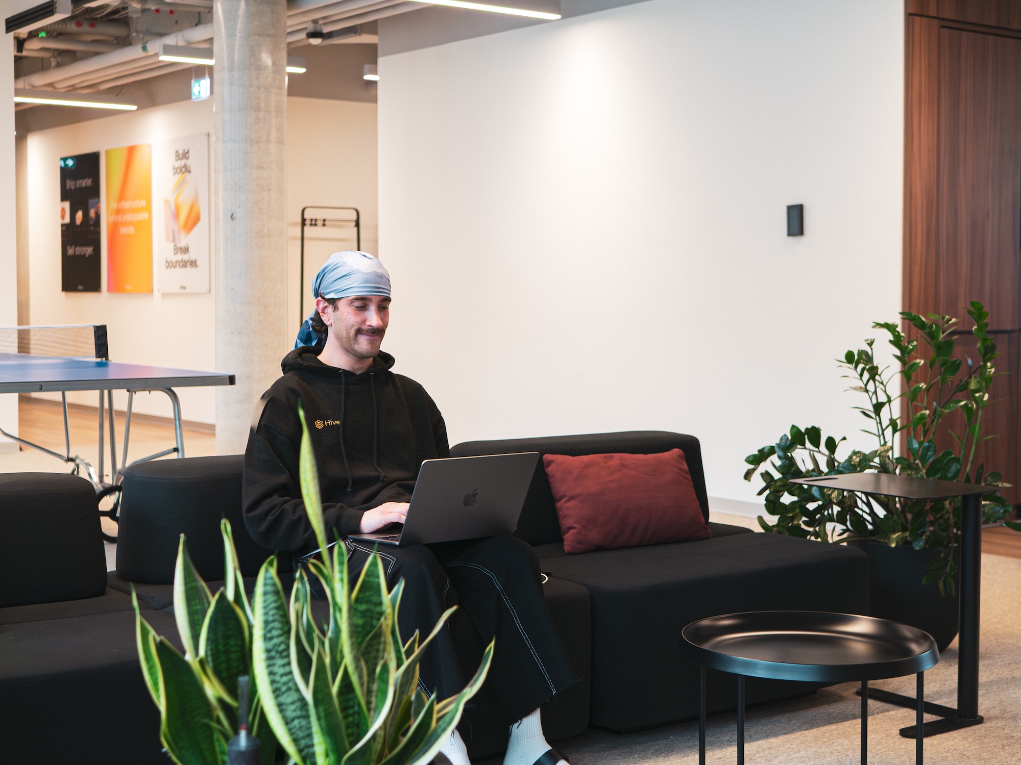 Hive employee working on a laptop on a NORNORM sofa near the office table tennis table