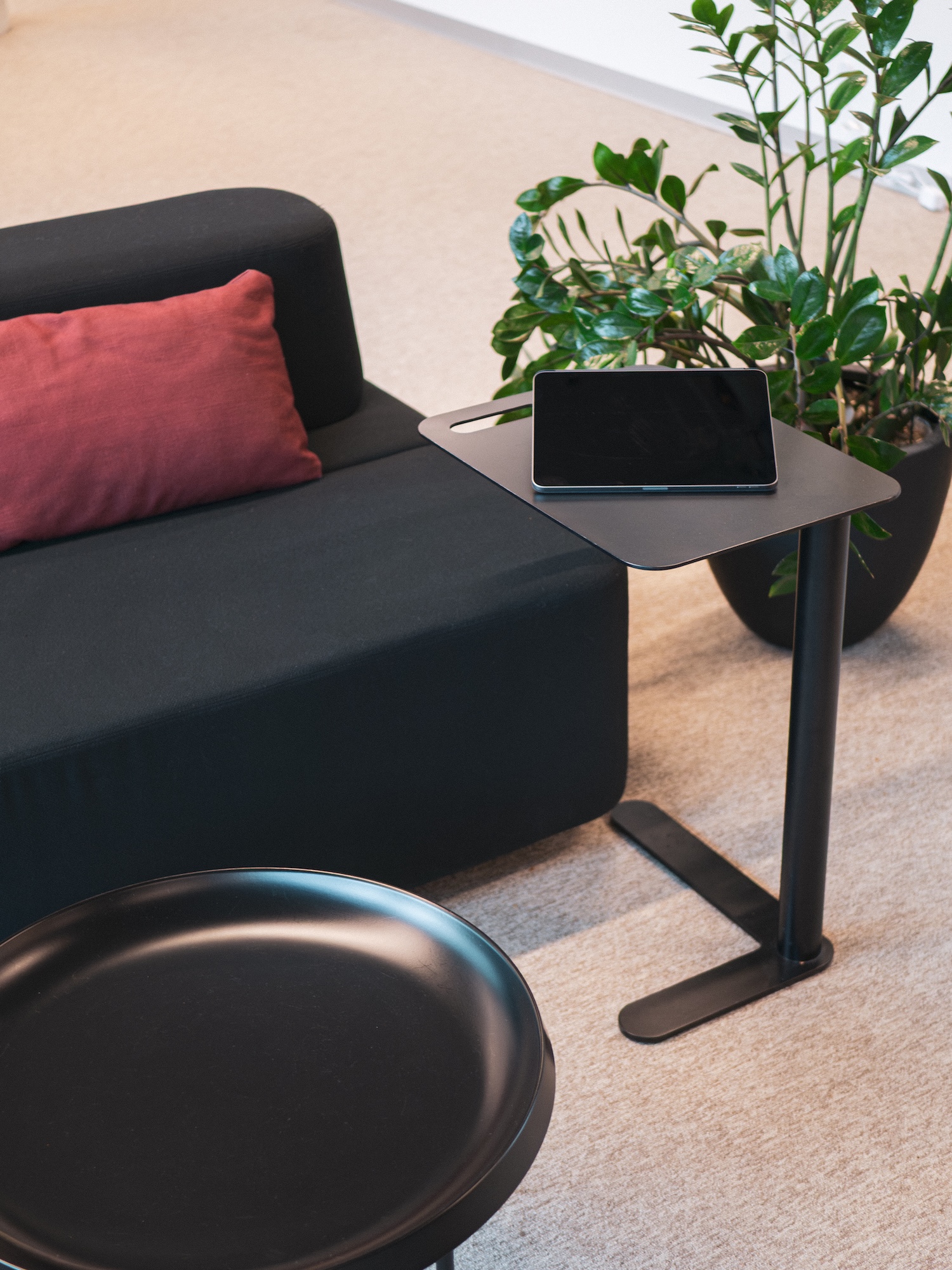 Close-up of a NORNORM side table holding a tablet beside a sofa and potted plant