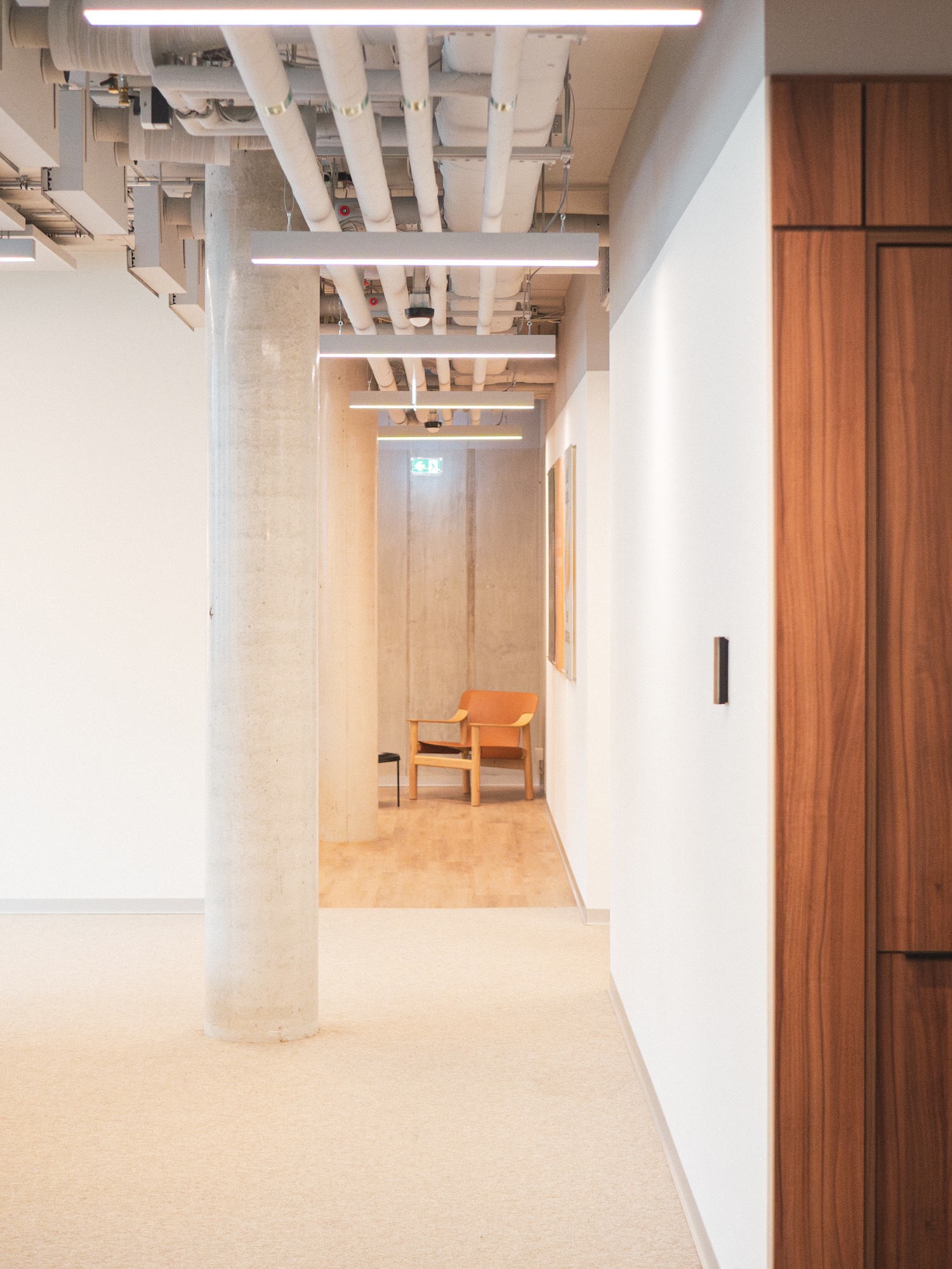 Corridor in Hive's Berlin office leading to a NORNORM lounge chair against exposed concrete