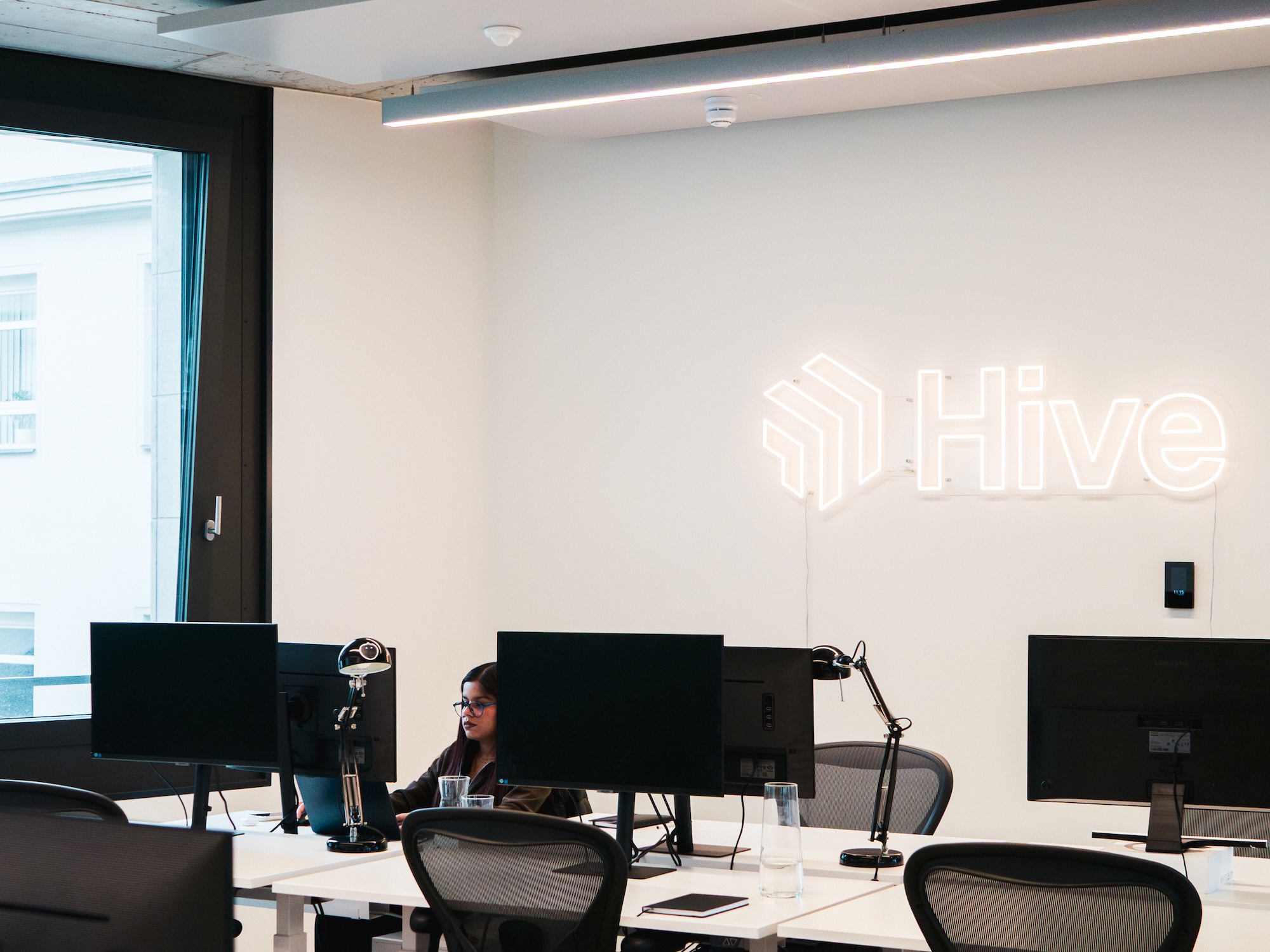 Hive employee working at a desk beneath the illuminated Hive logo in the Berlin office