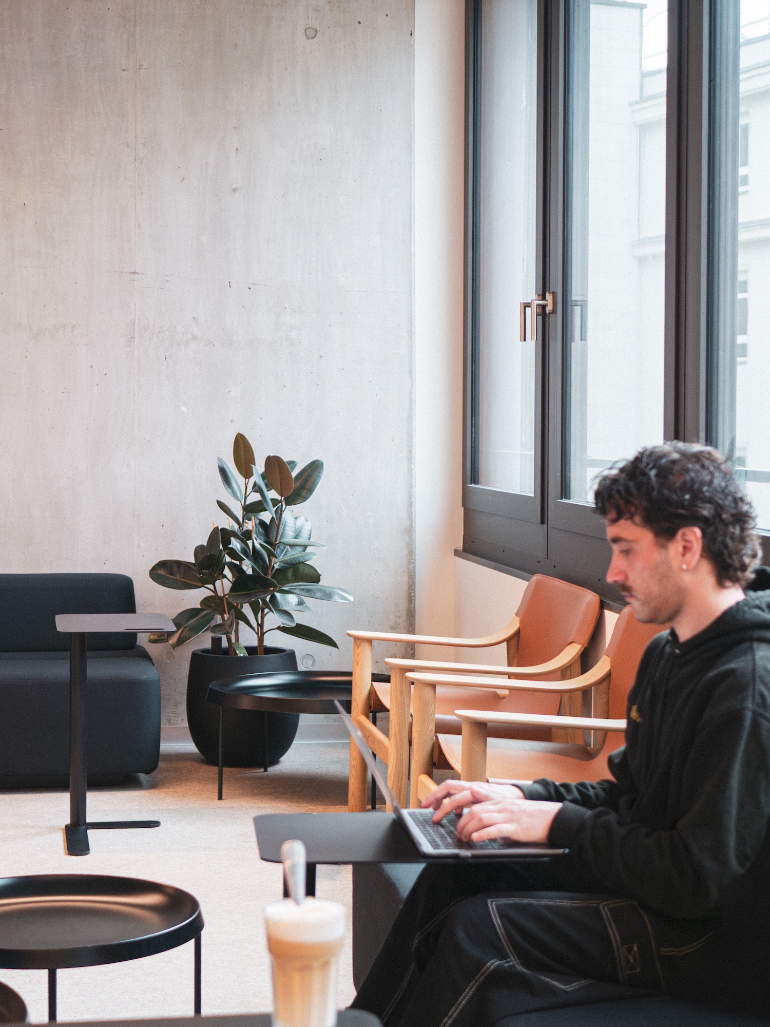 Hive team member on a laptop beside NORNORM lounge chairs and a rubber plant