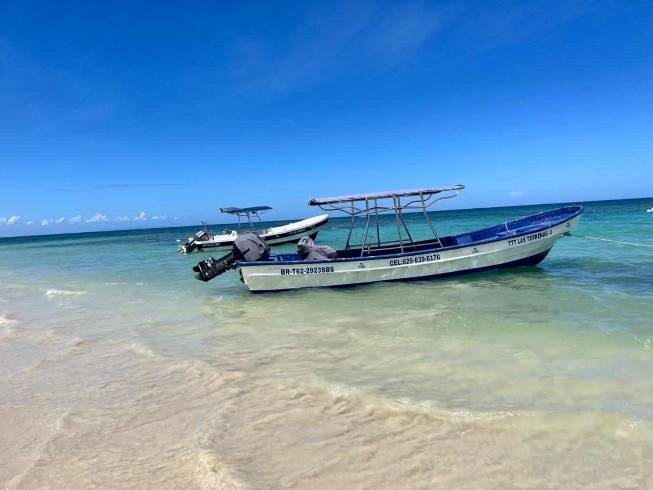 White and blue motorboat with two outboard engines floating on clear turquoise water, with blue cushioned seats and steering wheel, tethered by ropes.