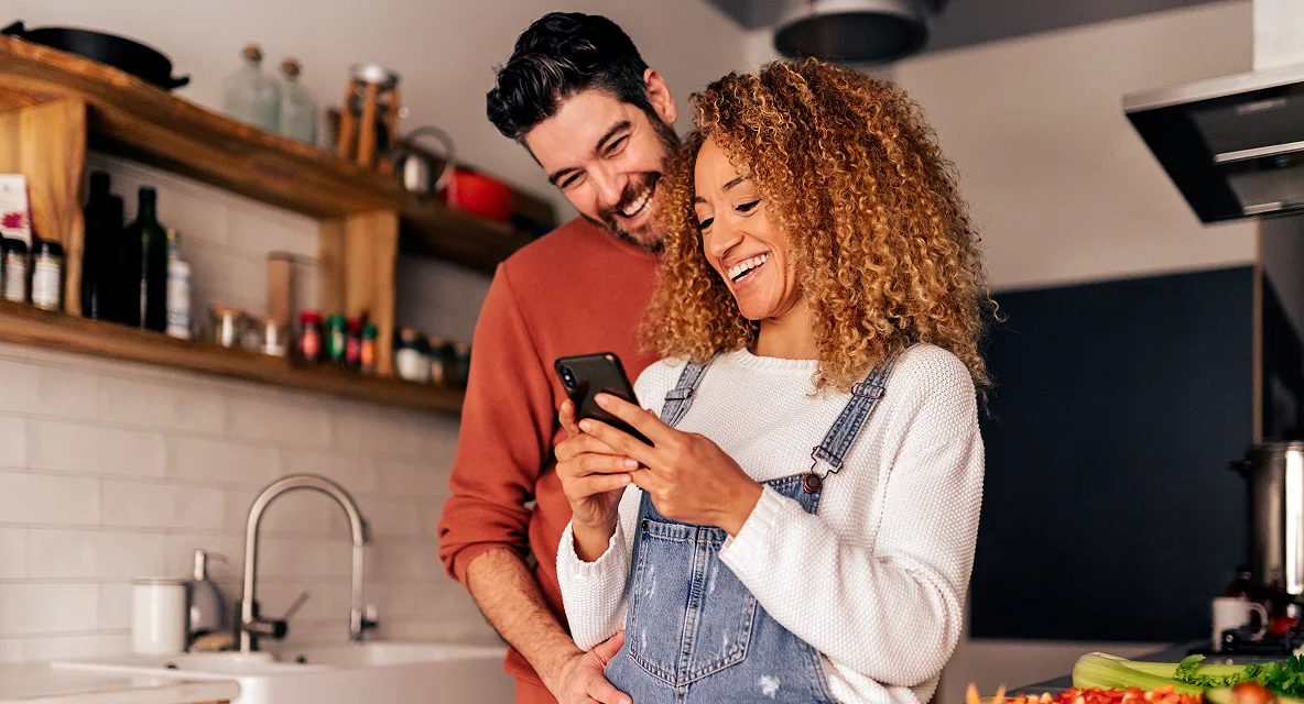 Smiling couple looking at a smartphone together in a modern kitchen.