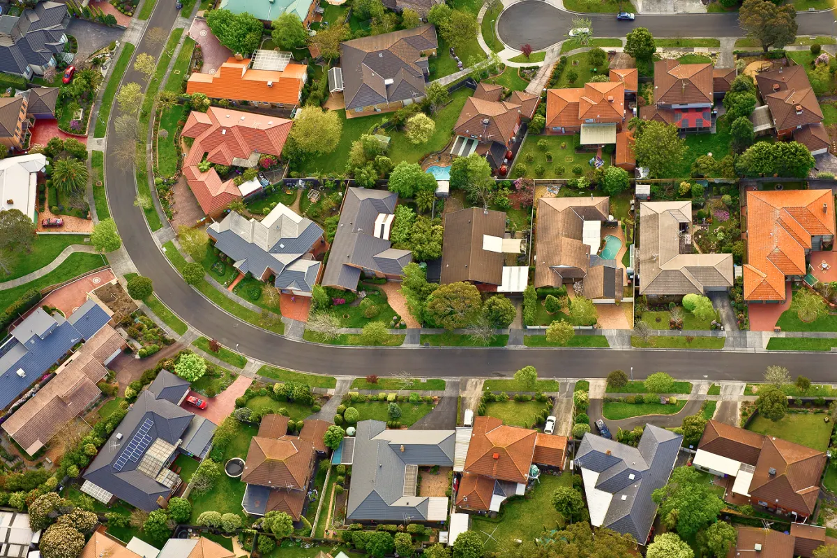 Aerial view of a suburban neighborhood featuring multiple detached houses with backyards, green lawns, and winding roads.