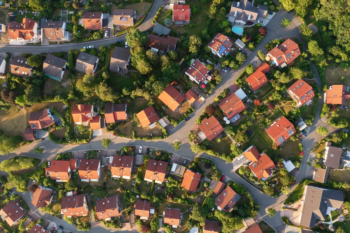 Aerial view of a suburban neighborhood with red-roofed houses, winding roads, and green trees and lawns.