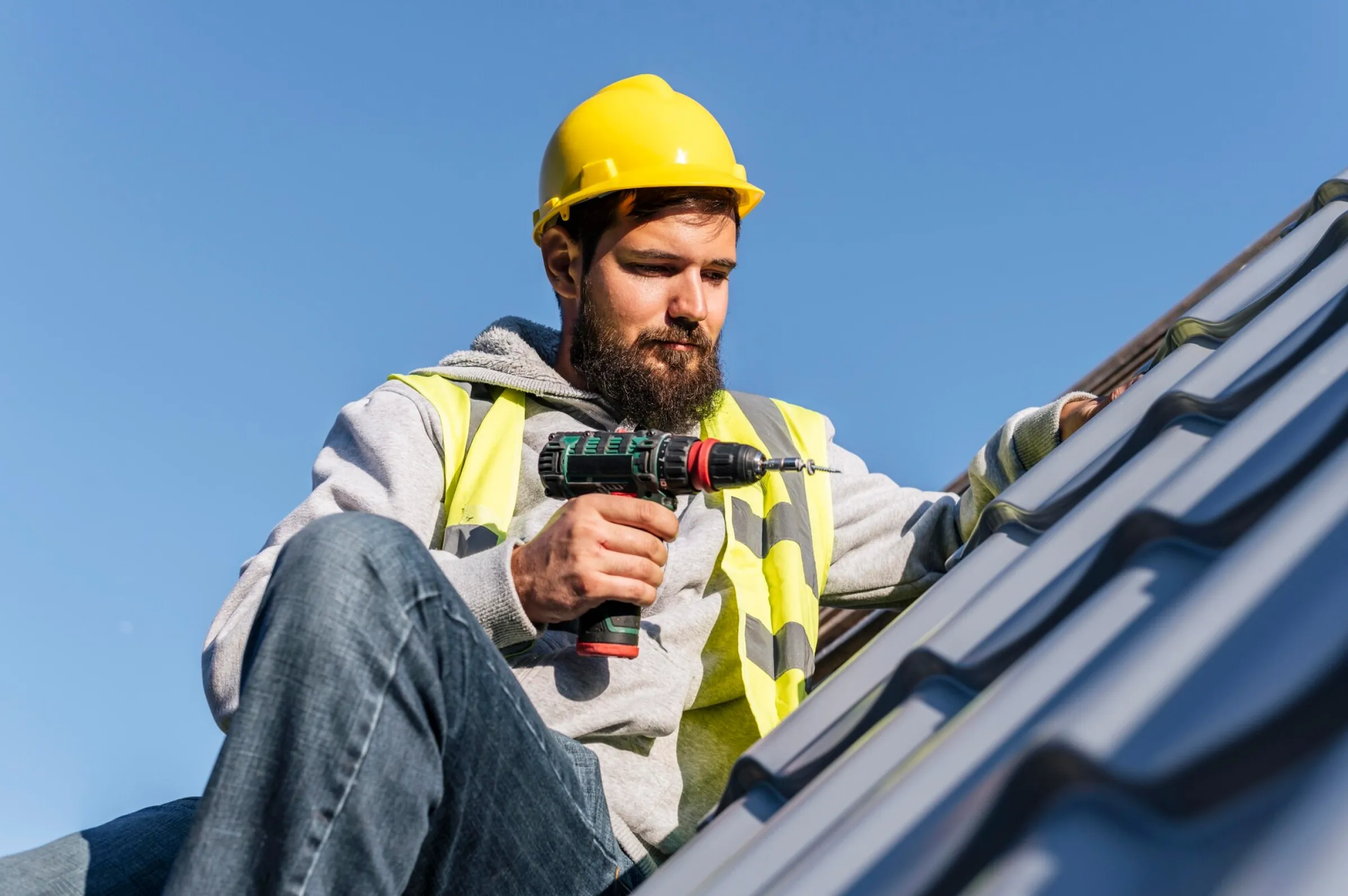 A man in a yellow hard hat is working on a roof.
