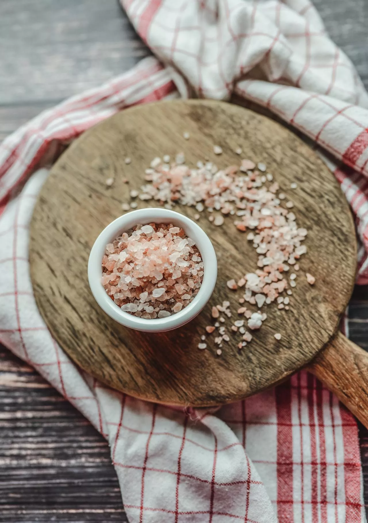 A wooden spoon with a white bowl of salt on a plaid cloth.