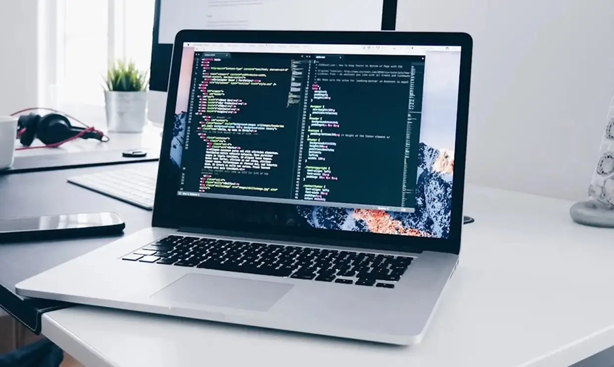Open laptop on desk displaying coding software with text editor and code on screen.