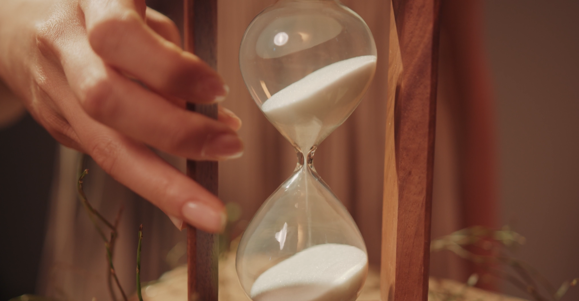 Photo of hand placed on an hourglass with sand flowing from top to bottom.