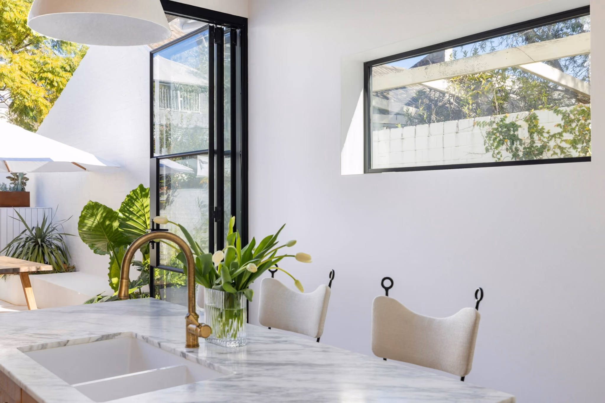 Open kitchen and courtyard connection with steel framed doors, marble island and soft natural light.