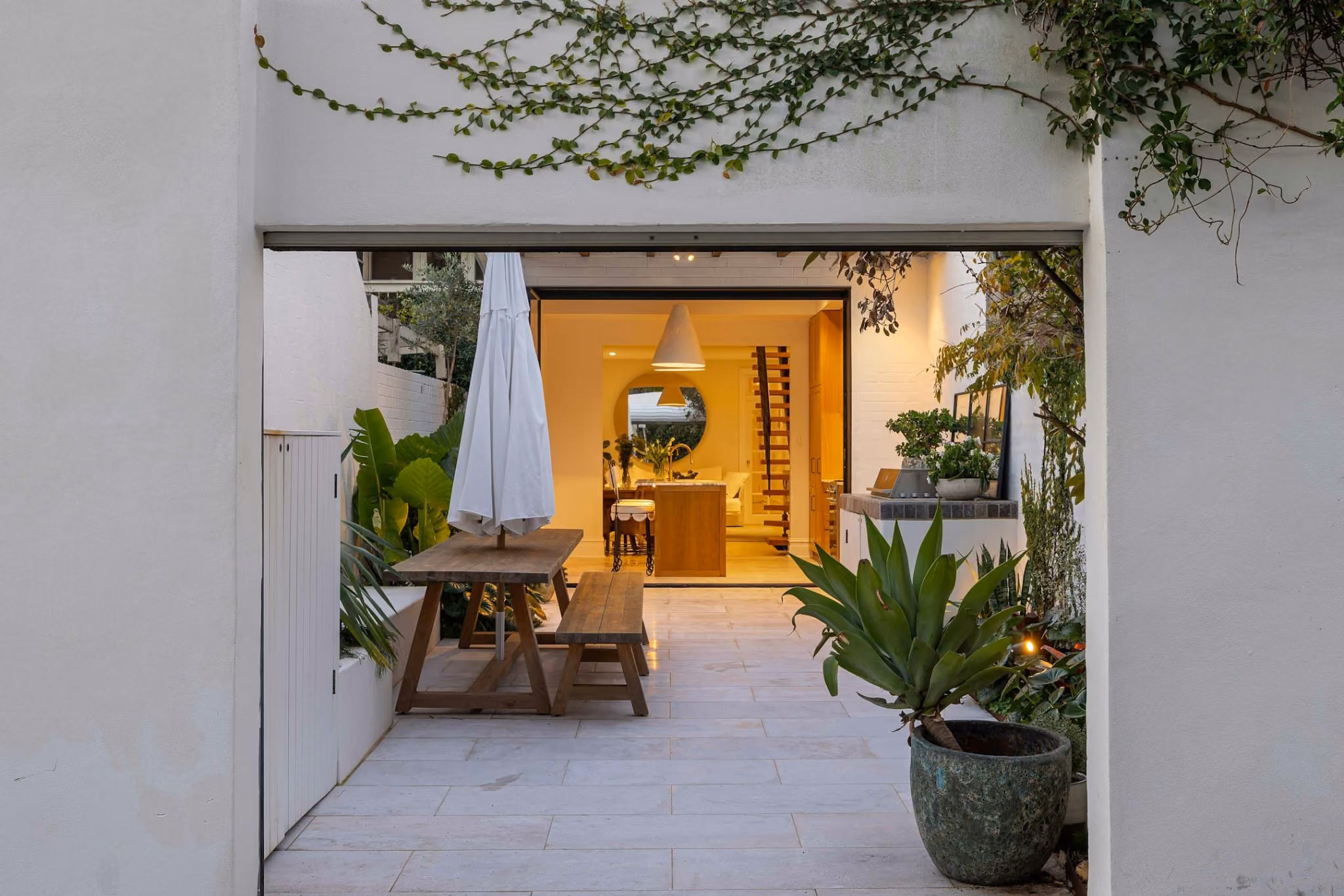 Twilight view of landscaped courtyard and rear extension with warm interior lighting and seamless indoor-outdoor connection.