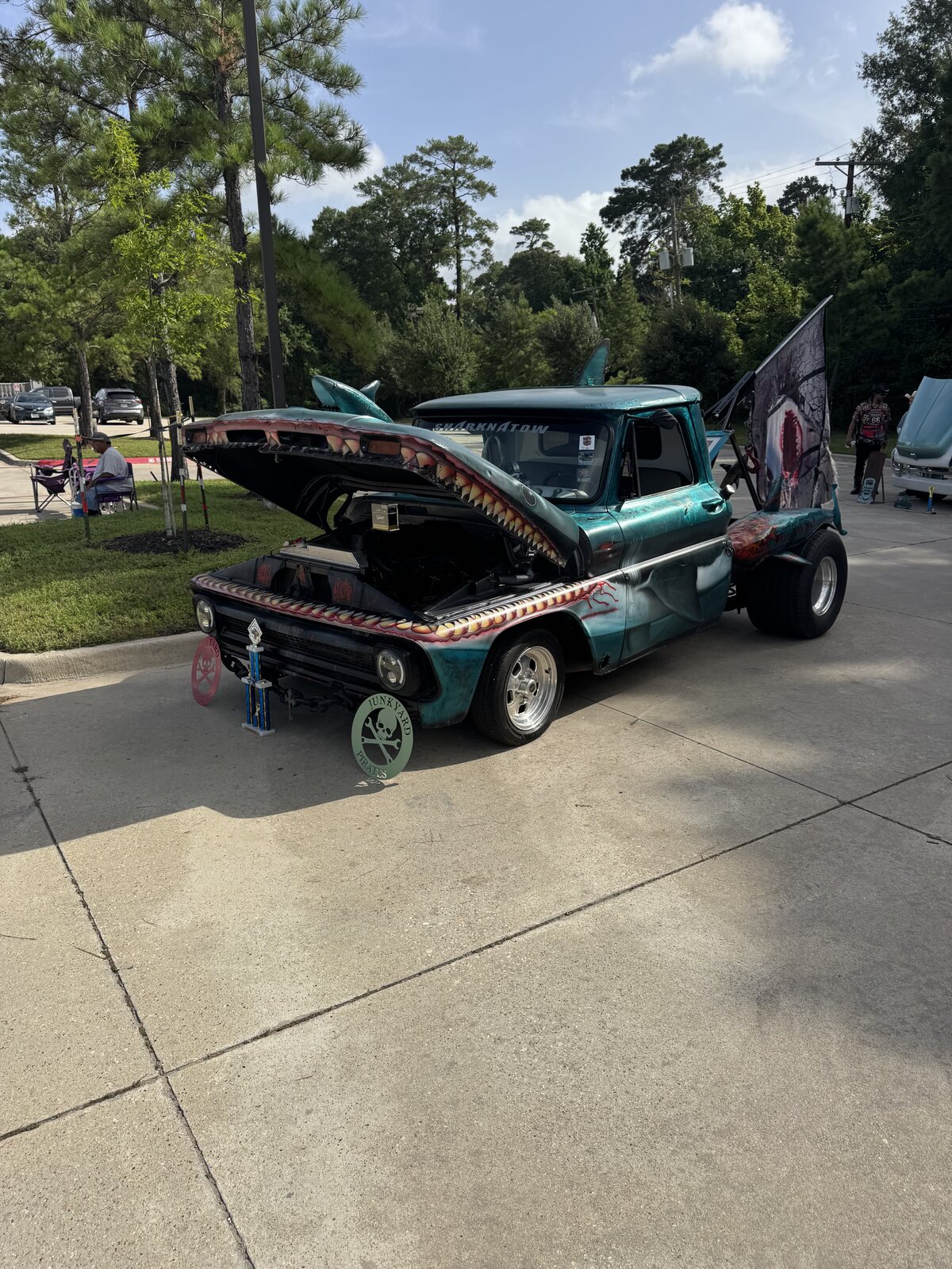 A teal shark-themed custom truck with a toothy shark-mouth grille and a fin on the roof at the Conroe car show