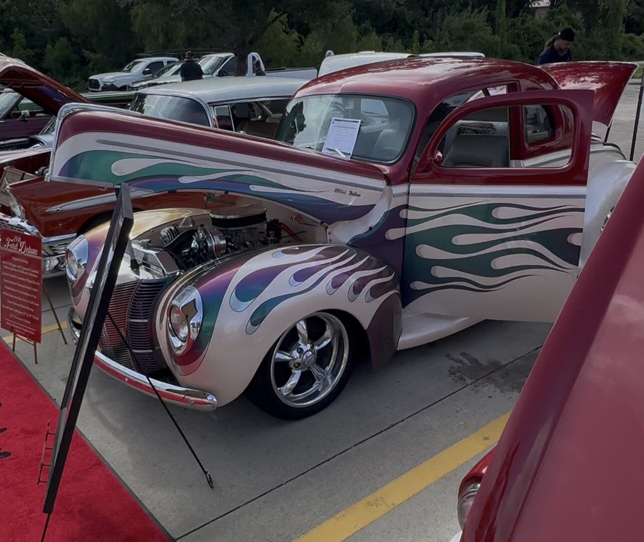 A 1940 Ford Deluxe hot rod with candy-colored flame paint and a polished blower on display in Conroe