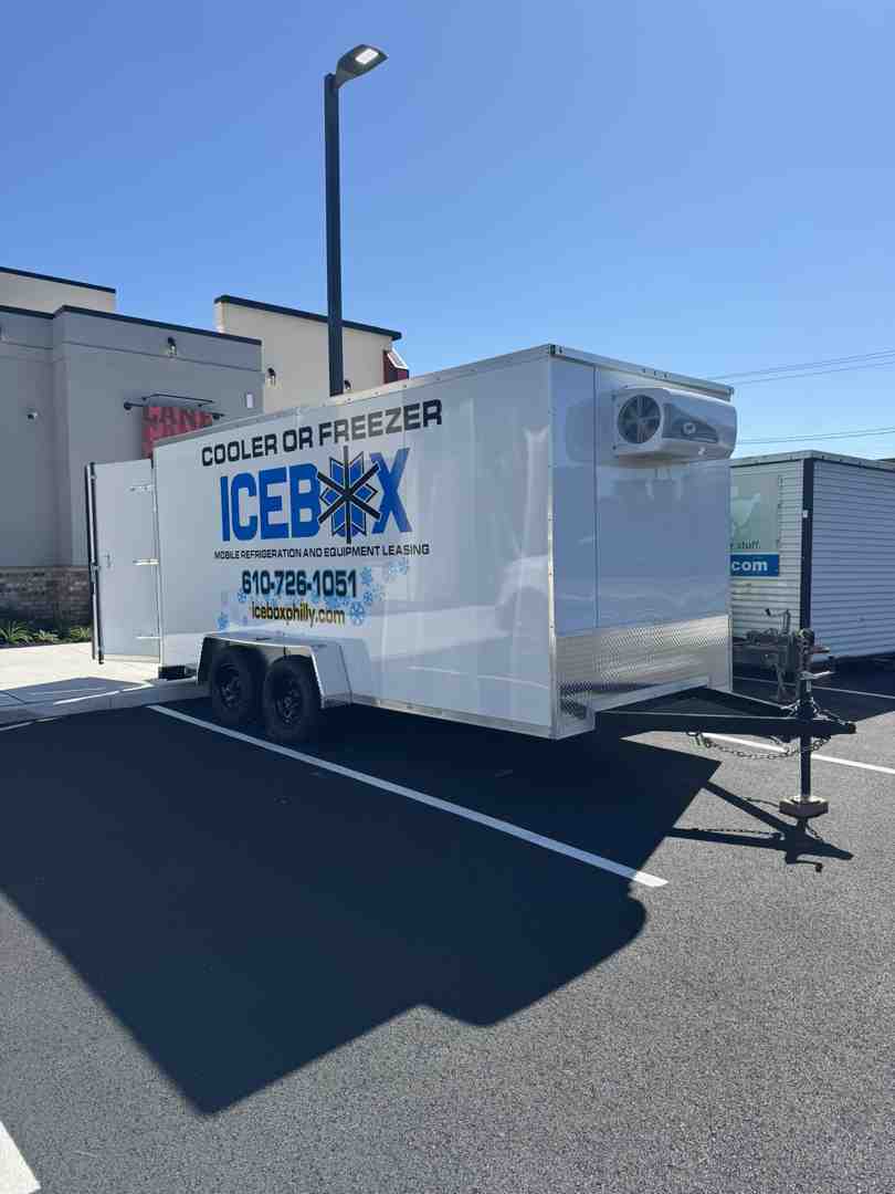 A clean, white mobile freezer trailer parked neatly in a restaurant parking lot, showing its compact size and easy accessibility - frozen storage unit