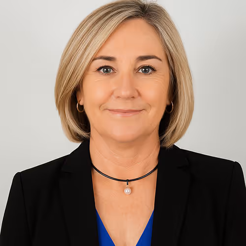 Professional headshot of a middle-aged woman with blonde hair wearing a black blazer and blue top, smiling softly.