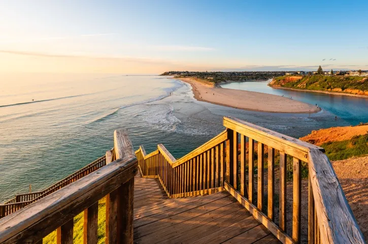 Wooden staircase leading down to a sandy beach and river mouth on a coastline at sunset.