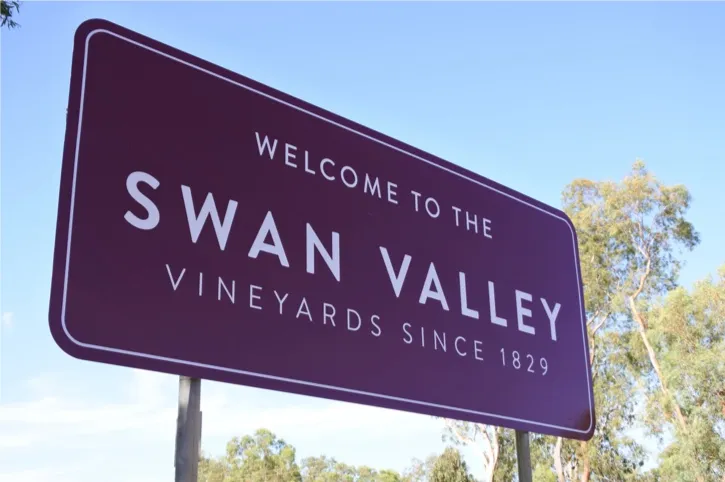 Sign reading 'Welcome to the Swan Valley Vineyards since 1829' against a clear blue sky with trees in the background.