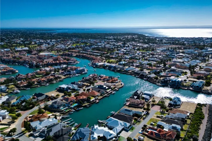 Aerial view of a coastal residential area with waterways and numerous houses under a clear blue sky.