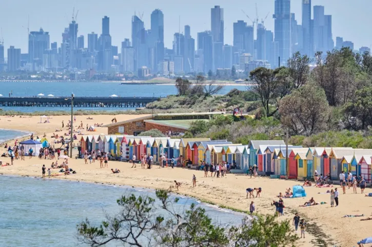 Brighton Beach in Melbourne with colourful bathing boxes along the sand and Melbourne city skyline in the background.