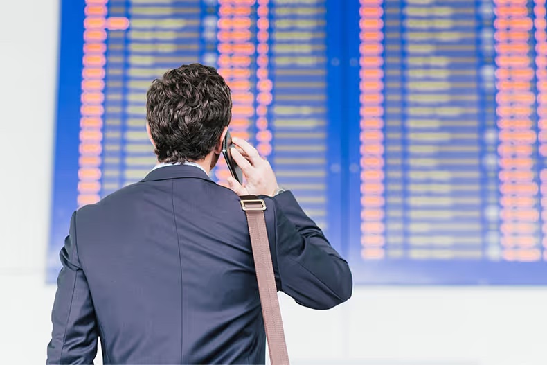 Traveller on the phone in front of an airport departures board