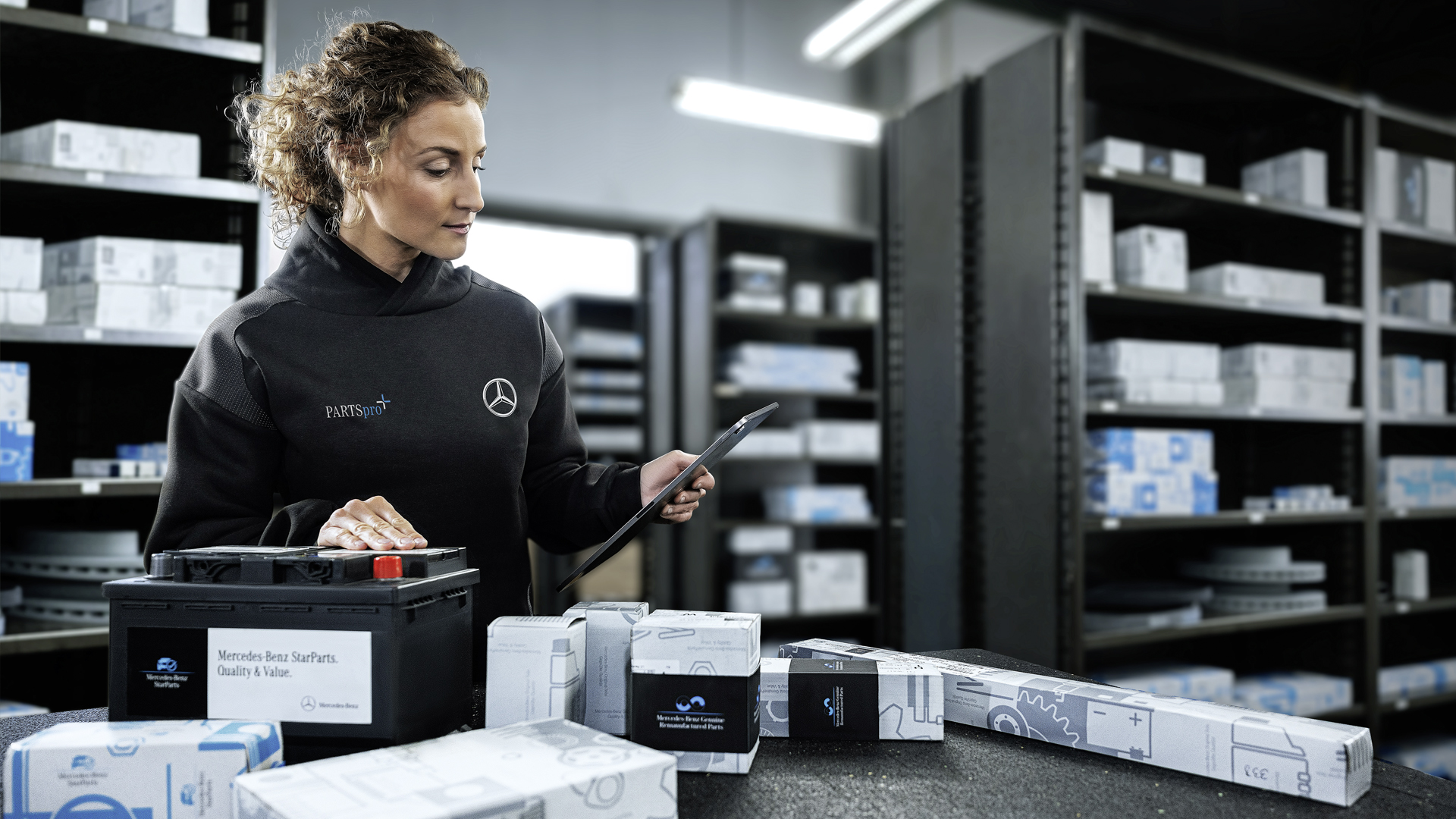 Mercedes-Benz Lager-Mitarbeiterin steht im Lager und packt Originalteile aus der Verpackung aus.