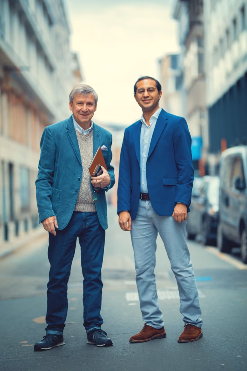 Un senior et un jeune homme en blazer bleu marine sont debout dans la rue et sourient en regardant le photographe