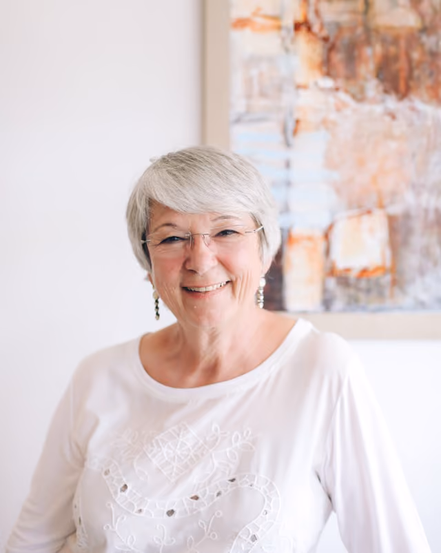 Portret van een vrouw met kort geknipt wit haar met een grote glimlach die naar de fotograaf kijkt.