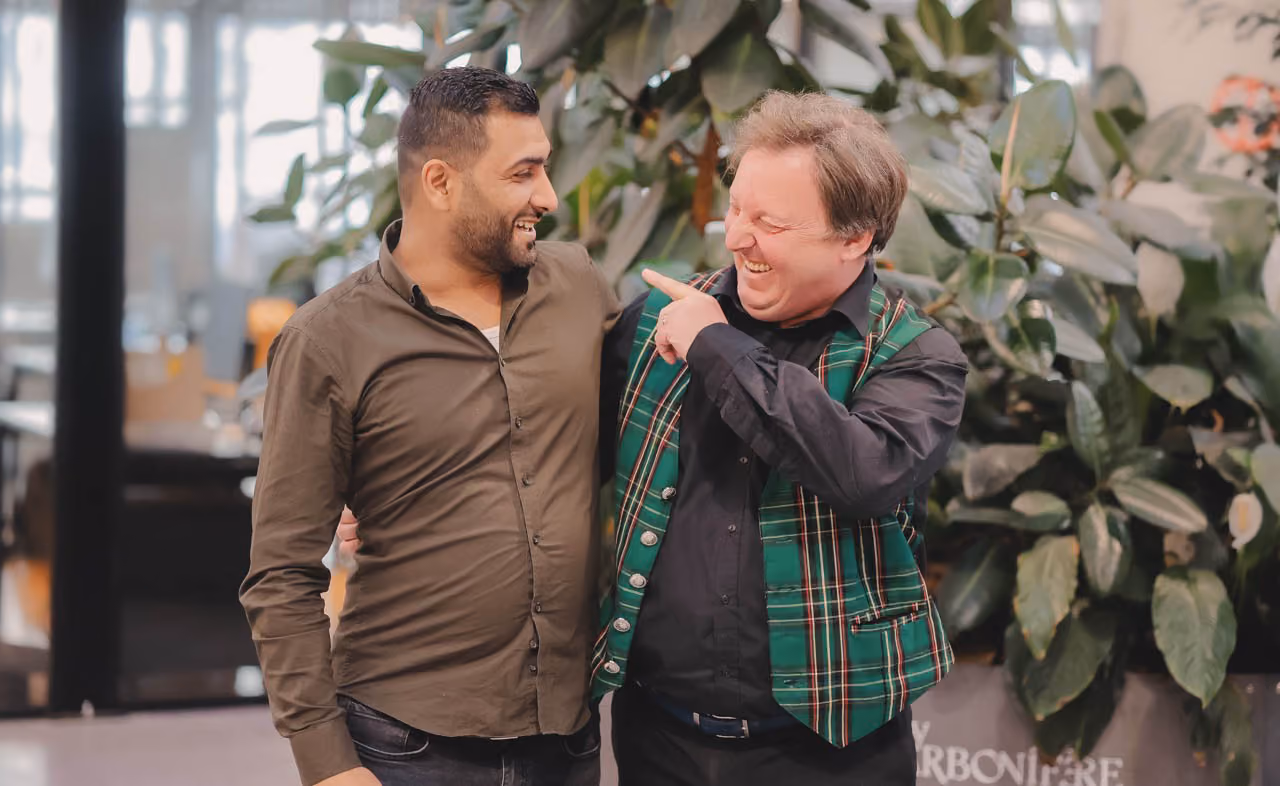 Un jeune homme d'origine moyen-orientale regarde en souriant son mentor avec un gilet écossais.